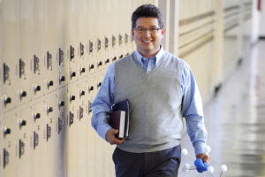 teacher in school hallway smiling wearing a gray vest
