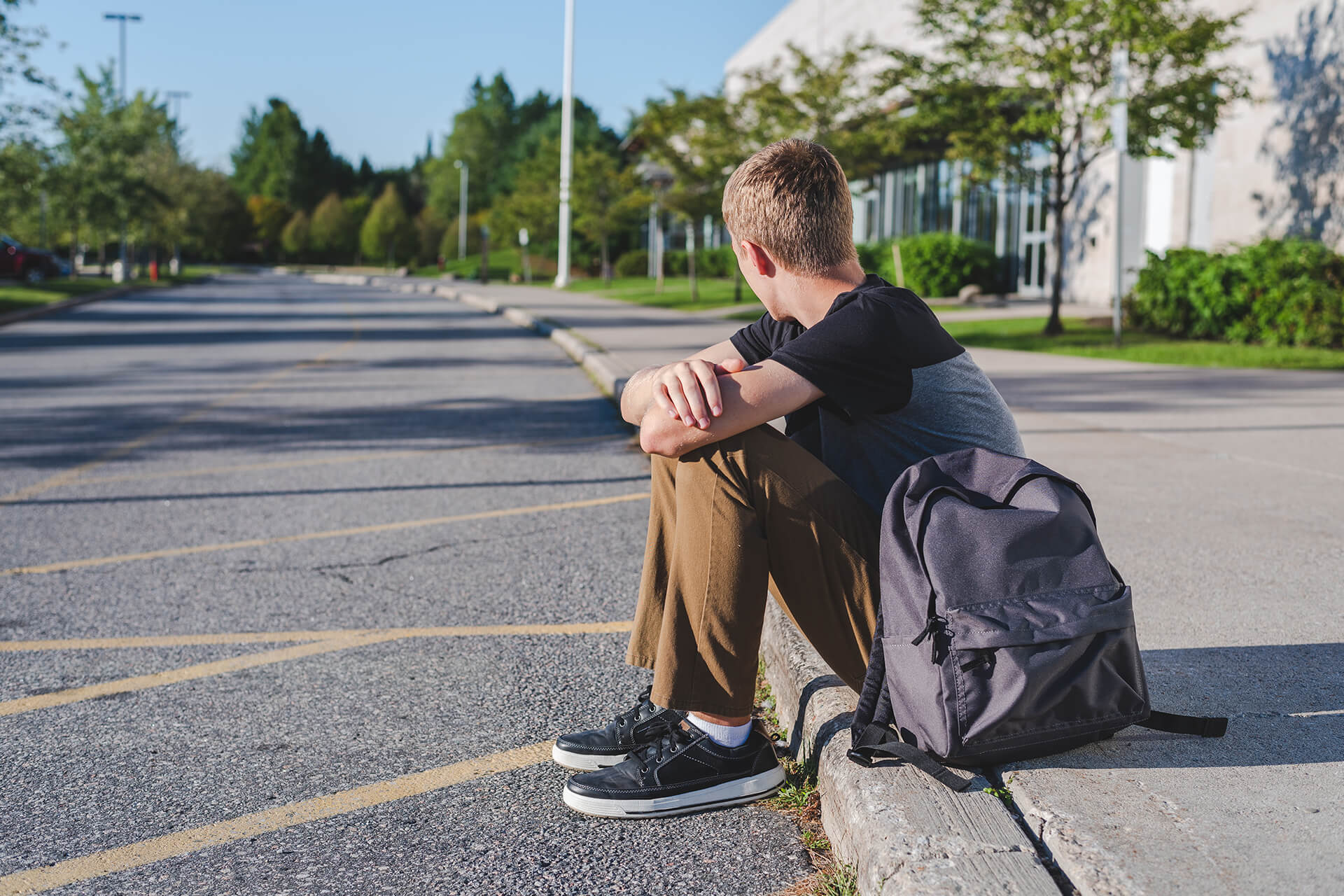 Boy sitting on curb in front of school waiting for a ride