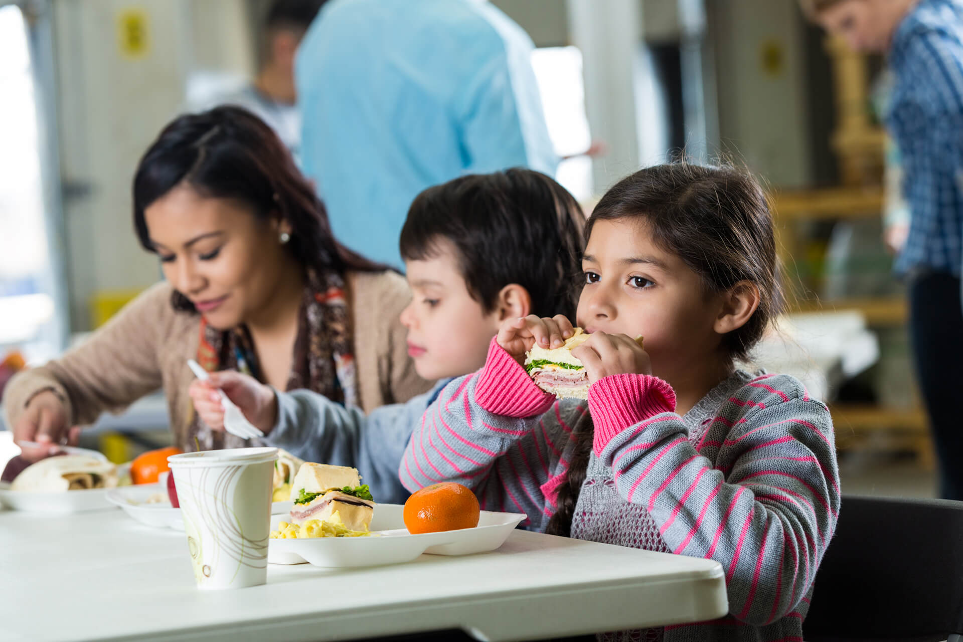 Child eating sandwich at table with mom and sibling