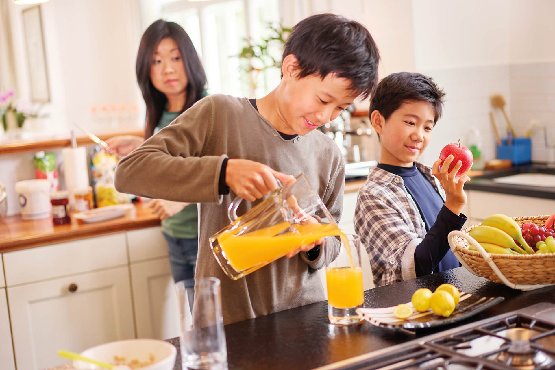 Teen pouring orange juice into glass in the kitchen with family